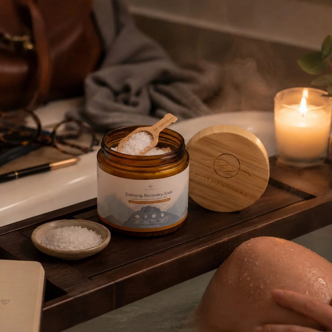 Evening Recovery Soak open on a wooden bath tray by candlelight, its scoop in the crystals and the bamboo lid beside it